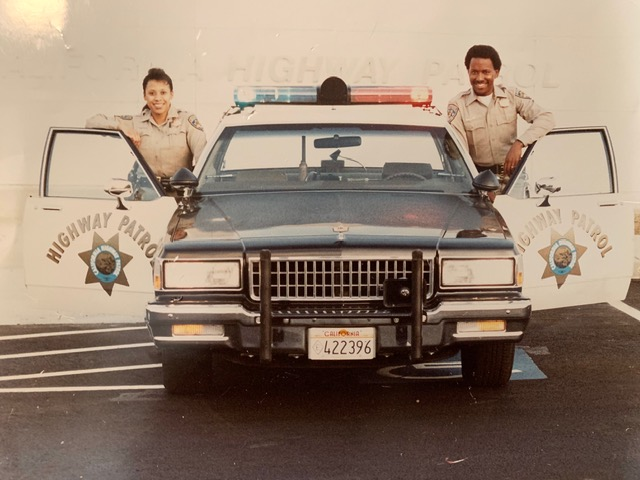 Two CHP officers standing in the open front doors of a black-and-white 1987 Chevrolet Caprice with a light bar: Michael Champion at the driver’s door and his car partner at the right front door.