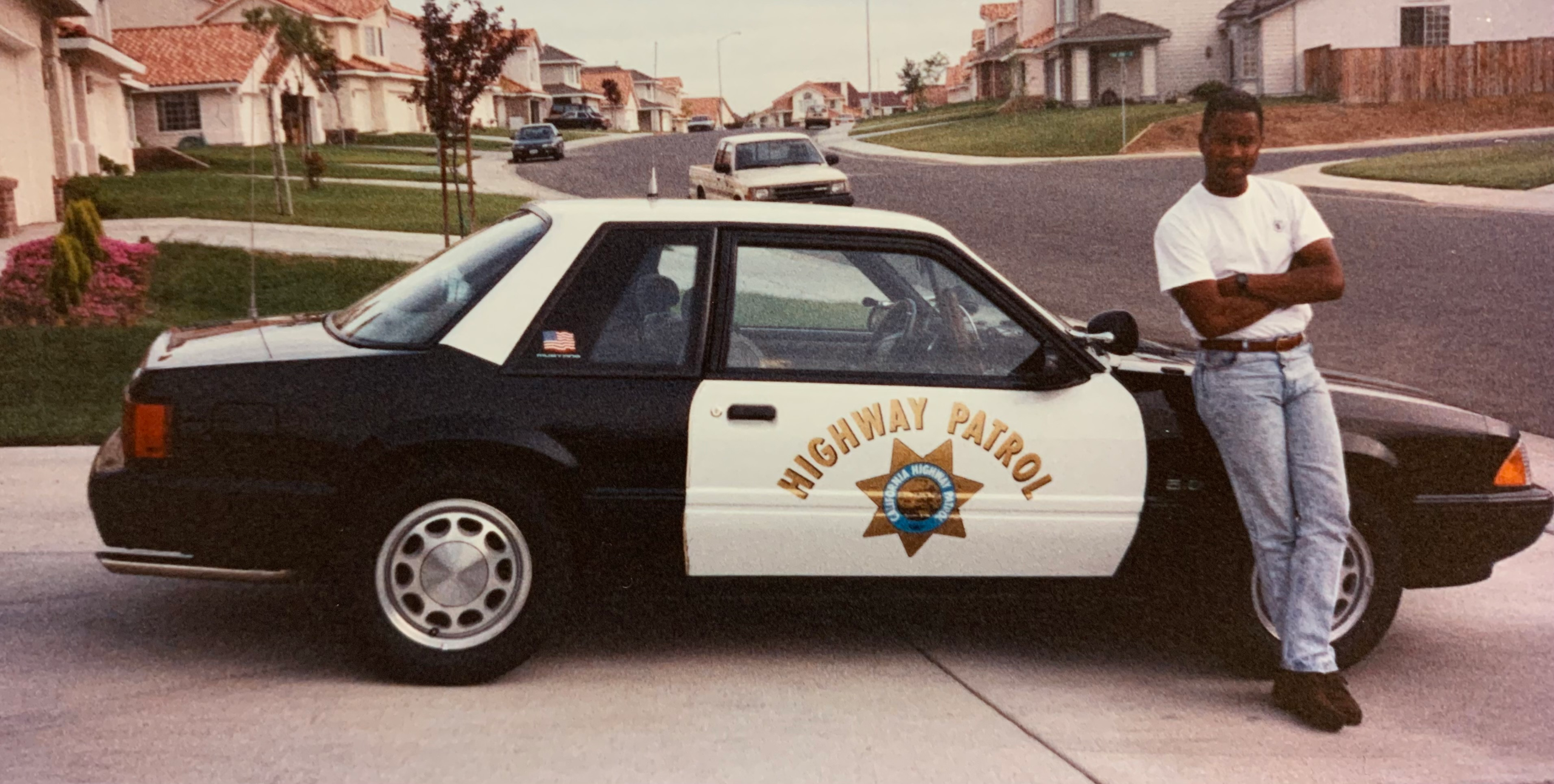 Michael Champion leaning against his black-and-white CHP Mustang SSP on a residential driveway, arms folded.